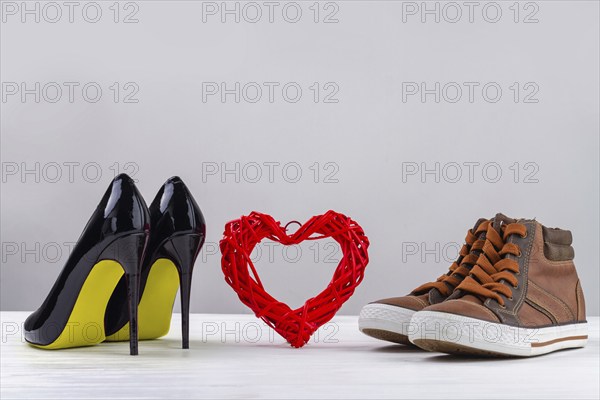 Red knitted heart with black womens high heel shoes and mens sneakers. Footwear on white background