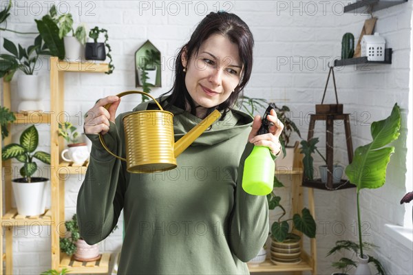 A portrait of a woman looks into the frame with an interior watering can and a spray gun for caring