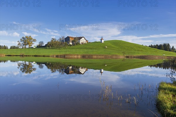 View of a lake with reflection of a house and a chapel on a hill, Hegratsrieder See near Füssen,