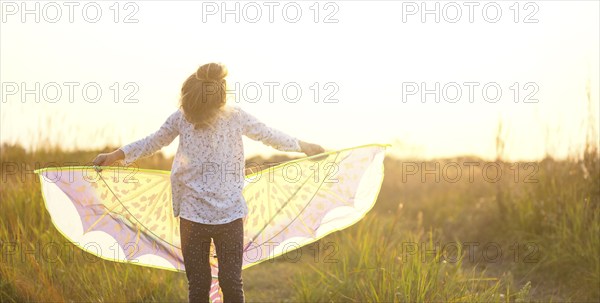 Girl is standing with wings in field, learning to fly a kite, Outdoor entertainment in summer,