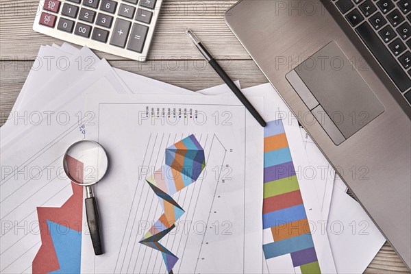 Papers with charts and glass magnifier with pen. Laptop device with calculator top view