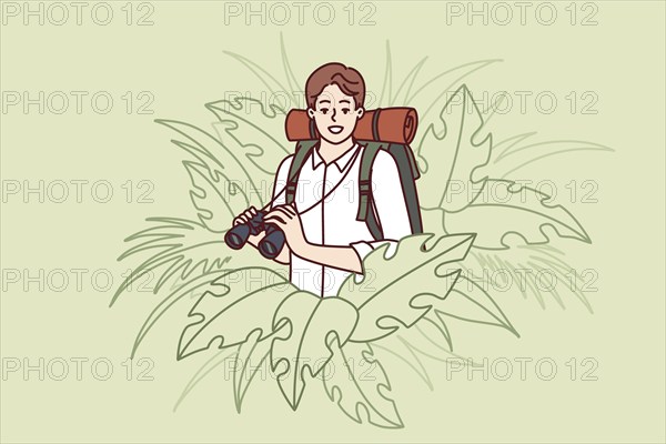 Man traveler stands in thickets of jungle and holds binoculars exploring area in search of further