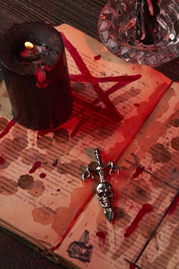 Vertical shot of antichrist cross on the satanic bible stained with blood. Burning black candle on