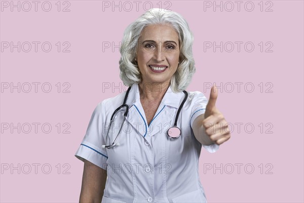 Successful senior woman doctor gesturing thumb up to camera. Joyful female doctor giving thumb up