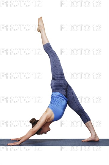 Woman doing Hatha yoga Eka pada adhomukha svanasana, one-legged downward facing dog on yoga mat
