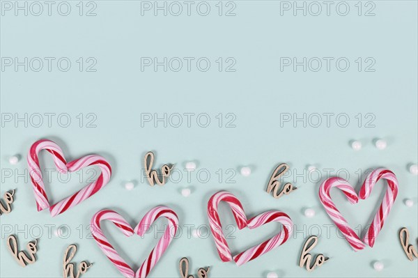 Small red and white striped Christmas candy cane sweets forming heart on blue background with copy