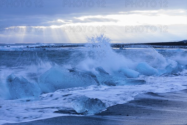 Waves breaking on icebergs on the black beach of Breidamerkursandur, near Jökullsarlon, Sudurland,