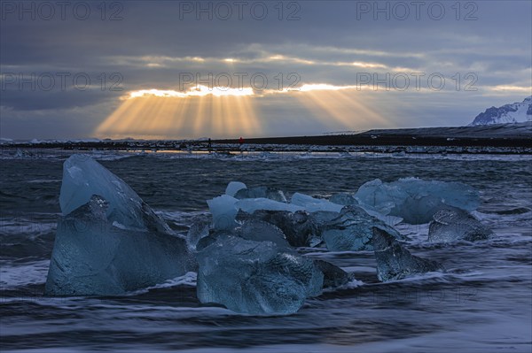 Waves breaking on icebergs on the black beach of Breidamerkursandur, sunset, near Jökullsarlon,