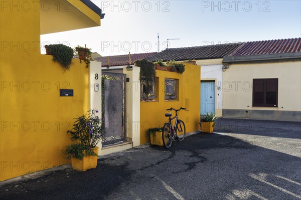 Potted plants and bicycle in front of a yellow house facade, Cabras, Oristano, Western Sardinia,