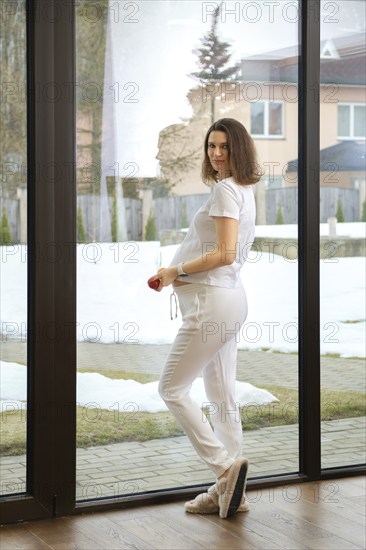 Beautiful pregnant woman standing by the window at home