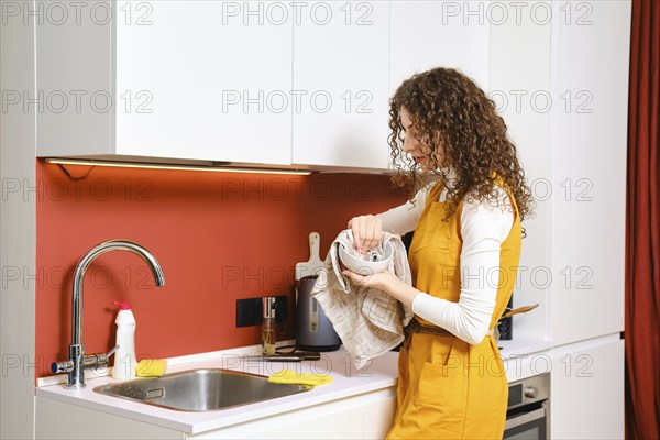 Young woman wipes plate with towel in the kitchen