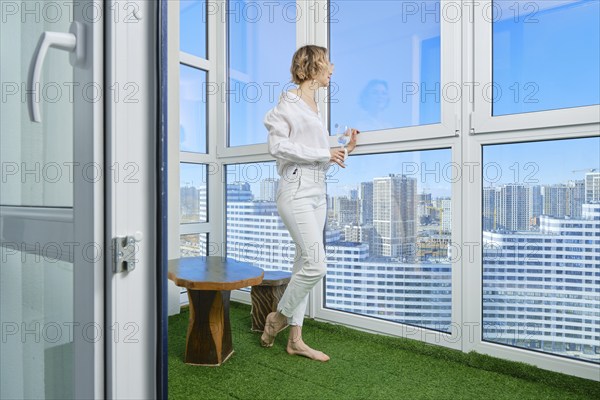 Barefoot woman stands on the balcony of her new apartment and admires the view of the city from the