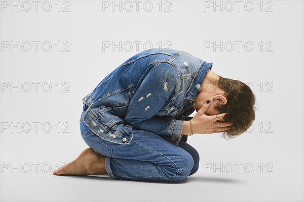 Desperate young man kneels on the floor and covers face with hands