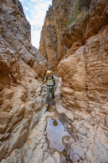 Mountaineers in a narrow canyon with a dry stream bed, eroded mountain landscape with red sandstone