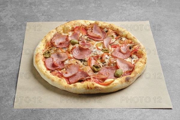 Pizza with ham, sausage, olives and bell pepper on parchment paper