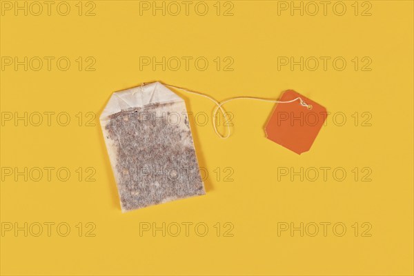 Tea bag with blank orange label on yellow background
