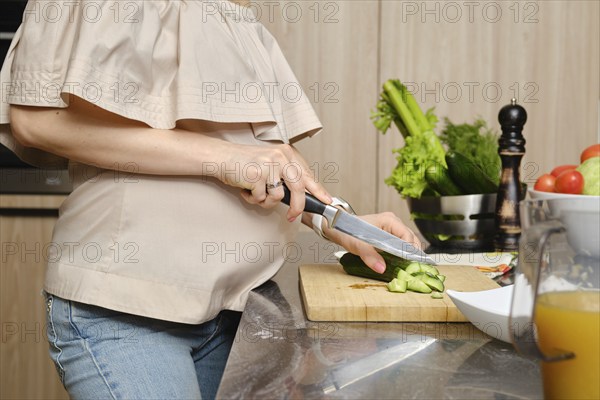 Closeup view of hands of pregnant unrecognizable woman in the kitchen cutting fresh and juicy