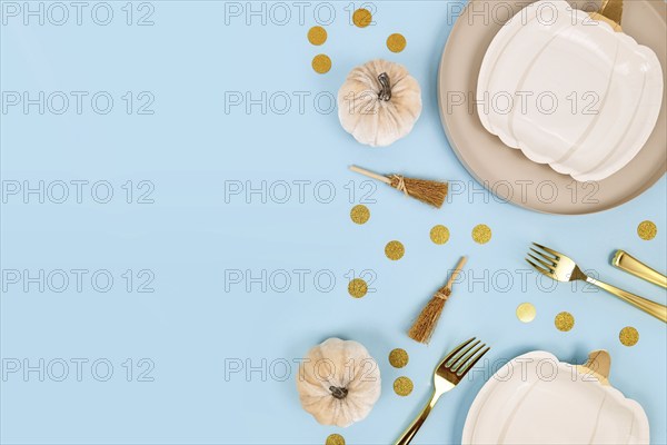 Halloween party flat lay with cream colored pumpkin shaped plates, witch brooms and golden confetti