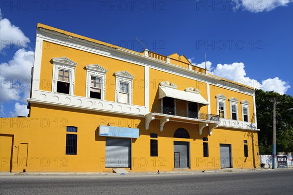 Two-storey yellow building under a clear blue sky with closed shop fronts, Church of Christ,