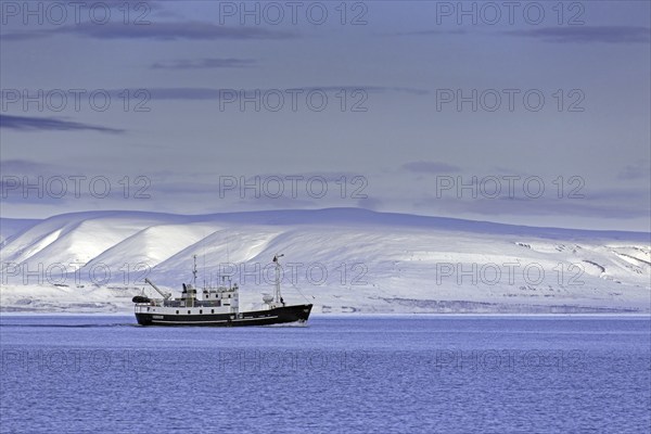 Snow covered mountains and boat with tourists during fjord-cruise in Billefjorden in autumn,