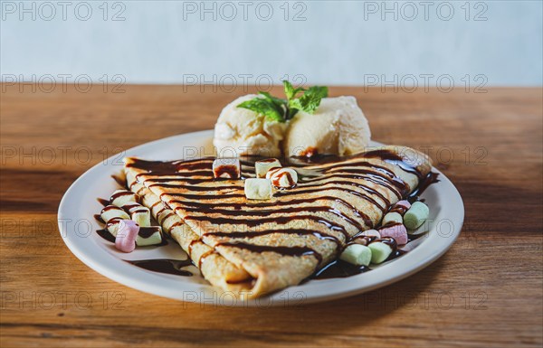 Close up of sweet crepe with ice cream on wooden table. Chocolate crepe with ice cream on wooden