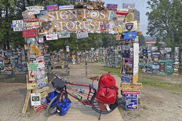 Bicycle with luggage in front of town and road signs in the signpost forest, cycling trip, cycling