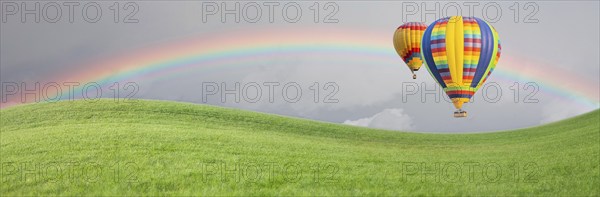 Hot air baloons drift above grass field with rainbow in the sky