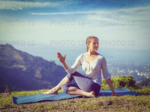 Yoga exercise outdoors, woman doing Ardha matsyendrasana asana, half spinal twist pose mountains in