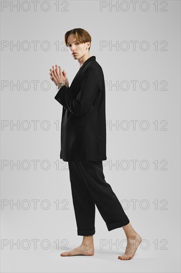 Young barefoot man in black suit posing in studio