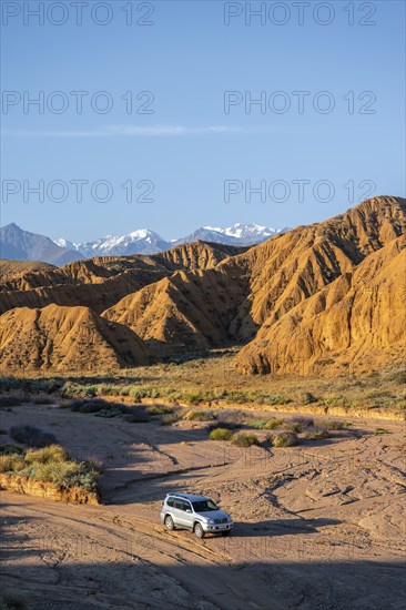 Off-road vehicle driving through a canyon, landscape of eroded hills at sunrise, badlands, white