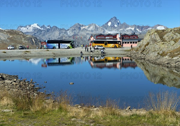 Coach with tourists and yellow bus of the Swiss PostBus AG on the Nufenen Pass, behind the mountain