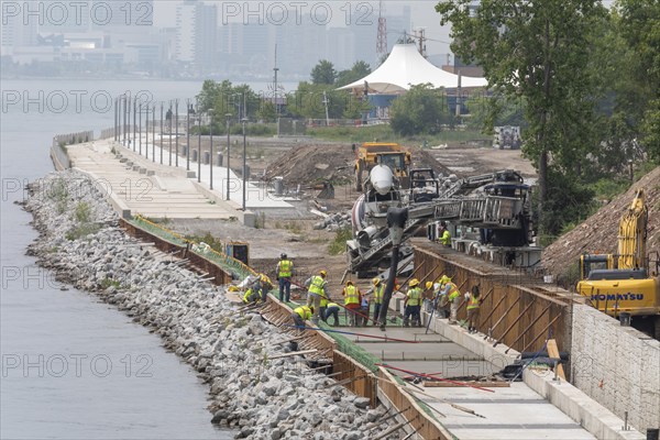Workers pour cement to complete a section of the Detroit Riverwalk on the site of the former