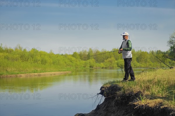 Man fish with spinning on river bank, casting lure. Outdoor weekend activity. Photo with shallow