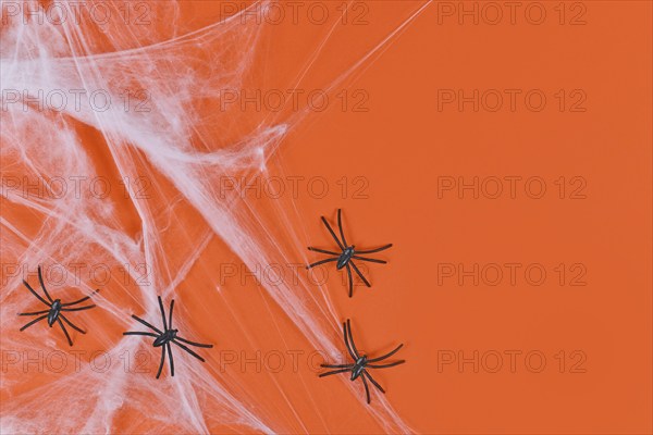 Cobweb and plastic spiders on side of orange Halloween background with empty copy space