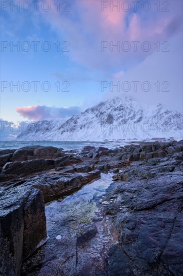 Beach of Norwegian sea on rocky coast in fjord on sunset in winter. Vareid beach, Lofoten islands,