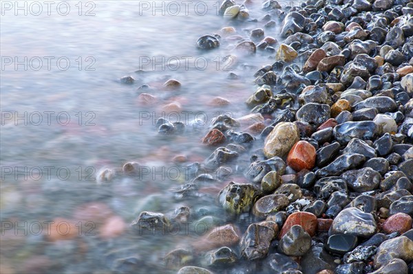 Blurred sea water of wave rolling over wet colourful pebbles on shingle beach, cobble beach