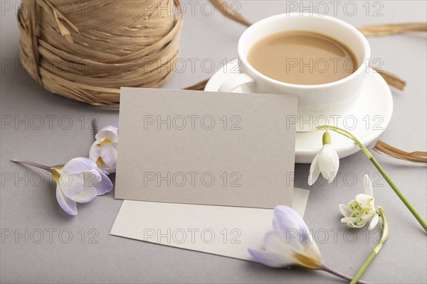 Gray paper business card mockup with spring snowdrop crocus and galanthus flowers and cup of coffee