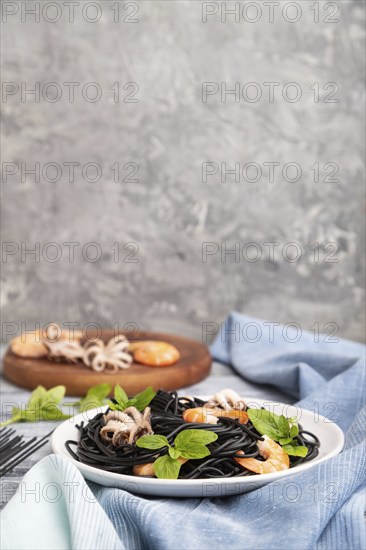 Black cuttlefish ink pasta with shrimps or prawns and small octopuses on gray wooden background and