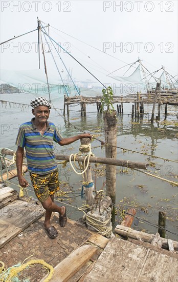 Indian fisherman standing at Chinese fishing nets, behind the Arabian Sea, Kochi, Kerala, India,