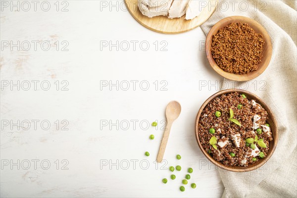 Quinoa porridge with green pea and chicken in wooden bowl on a white wooden background and linen
