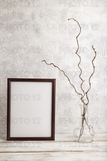 Brown wooden frame mockup with dried wine branch in glass on gray concrete background. Blank,