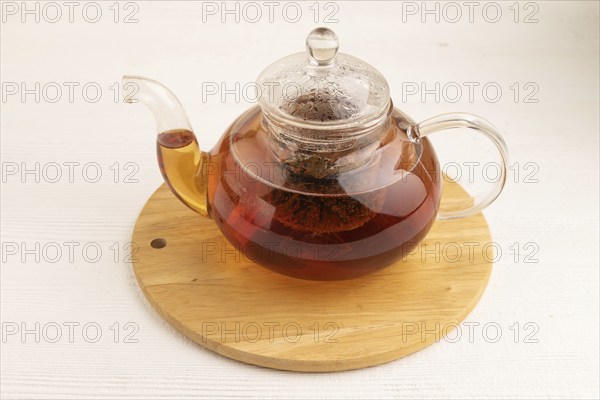Red tea with herbs in glass teapot on white wooden background. Healthy drink concept. Top view,