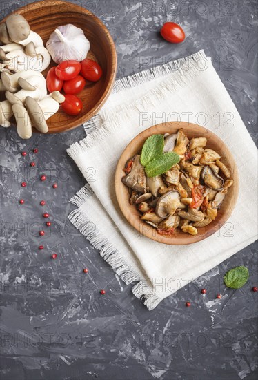 Fried oyster mushrooms with tomatoes in wooden plate on black concrete background. top view, copy