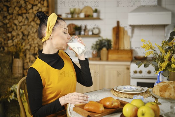 Woman drinking milk while sitting at the table in rustic style kitchen. The table is served with