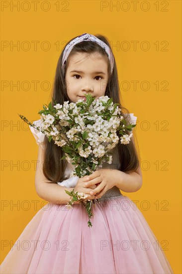 Cute young girl with bouquet of spring flowers over yellow background