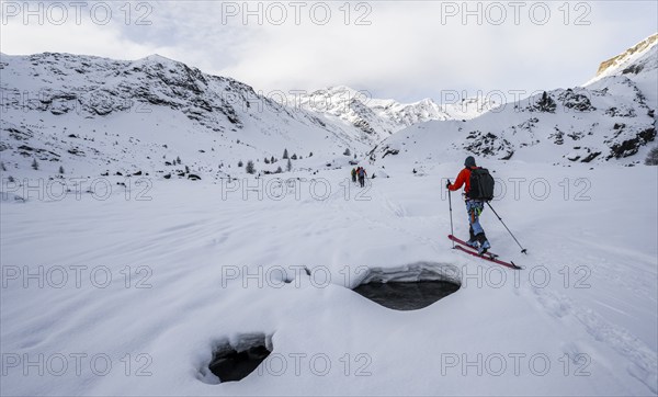 Ski tourers ascending in the rear Martell Valley, snow-covered mountain peak Monte Cevedale behind,