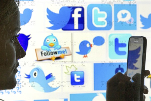 Silhouette of a woman with a smartphone in her hand in front of a Facebook and Twitter logo,
