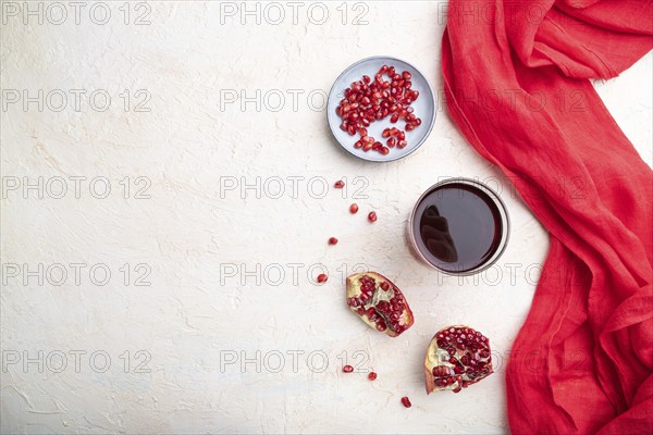 Glass of pomegranate juice on a white concrete background with red textile. Top view, copy space,