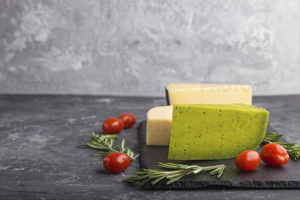 Green basil cheese and various types of cheese with rosemary and tomatoes on black slate board on a