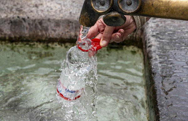 Water fountain, a woman fills drinking water into a small plastic bottle, Munich, Bavaria, Germany,